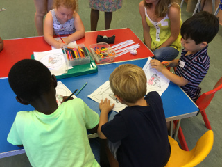 A girl and three boys doing some colouring at a table with a helper