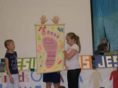 Child holding a banner of a footprint with two girls looking on