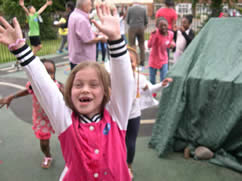 Happy girl holding her hands up in a playground among other children and adults