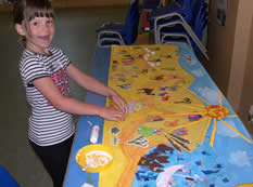 Girl looking at a picture on a table of a map with boat and sun