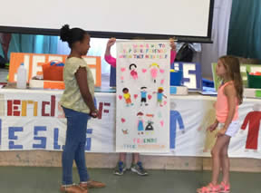 Girl hidden behind a banner with human figures holds it up while two other girls look on