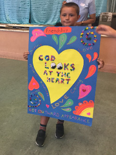 A boy holds a poster of a yellow heart with the words 'God looks at the heart'