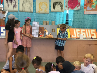 Three girls and a boy holding a cardboard scene of Paul, Silas and the jailor